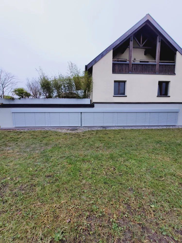 Haus mit Giebel und Lamellenstoren im Obergeschoss