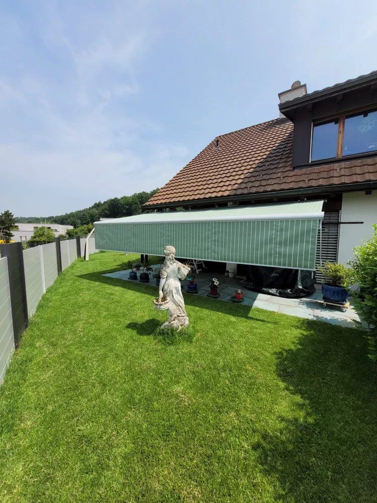Grüne Markise am Haus mit Gartenstatue