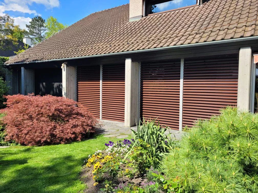 Braune Rollläden an einem Haus mit Garten